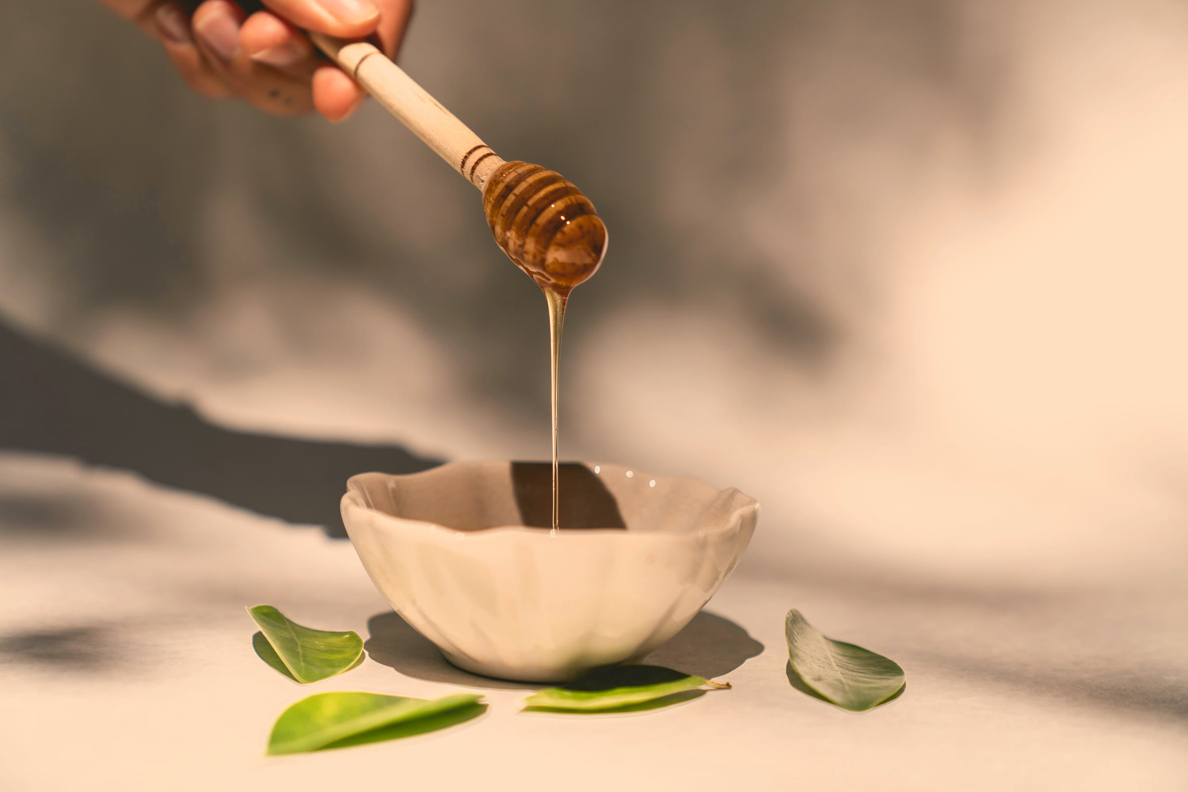 Honey poured from a wooden dipper into a ceramic bowl